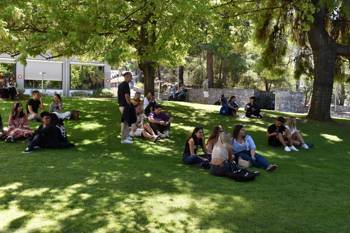 A group of students relaxes on the grassy area of a college.